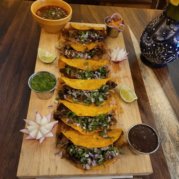 Monte Alban Restaurant's birria tacos with consommé, salsa, lime, and radish on a wooden board.