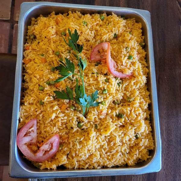 Mexican rice with peas, carrots, parsley, and tomato slices in a metal serving pan.