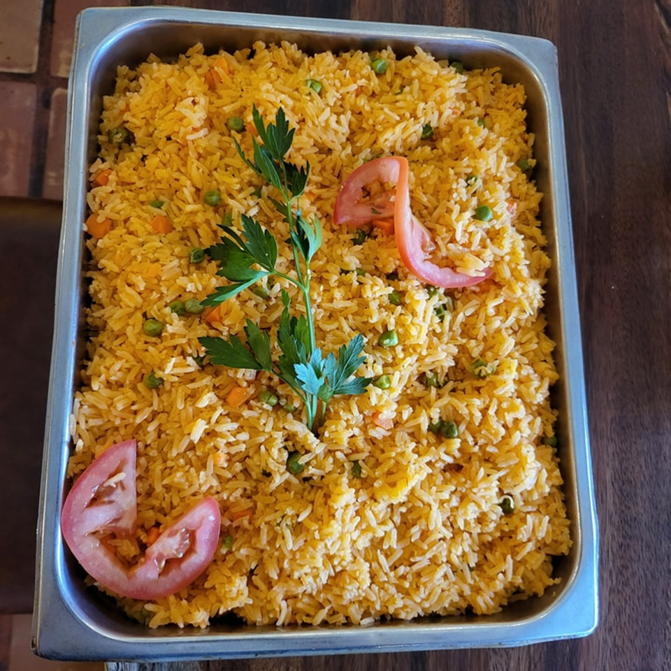 Mexican rice with peas, carrots, parsley, and tomato slices in a metal serving pan.