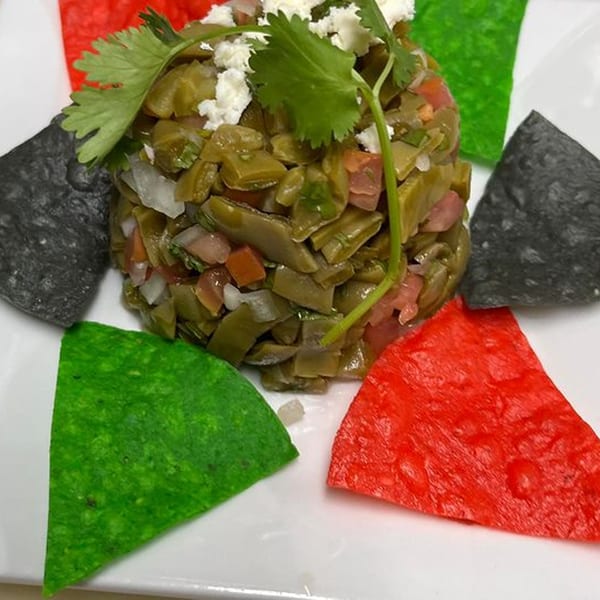 Nopal salad with cilantro and cheese, surrounded by red, green, and black tortilla chips.