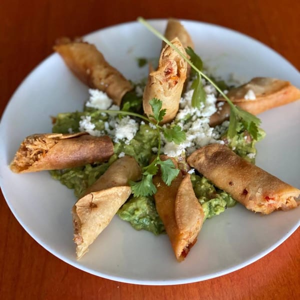 Crispy taquitos arranged on a bed of guacamole, topped with crumbled cheese and cilantro.